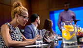 3 colleagues sit at a conference table as a fourth coworker makes a presentation using a video screen
3 colleagues sit at a conference table as a fourth coworker makes a presentation using a video screen