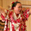 A woman in Hawaiian garb and a group of children sitting on the floor watching her reach to the sky